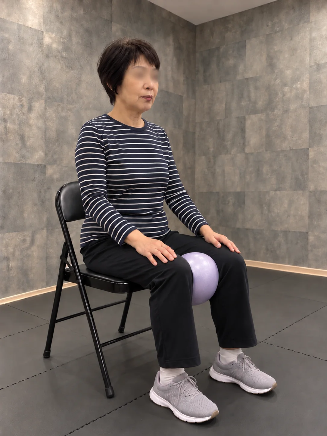 椅子に座って膝の間にボールを挟む女性