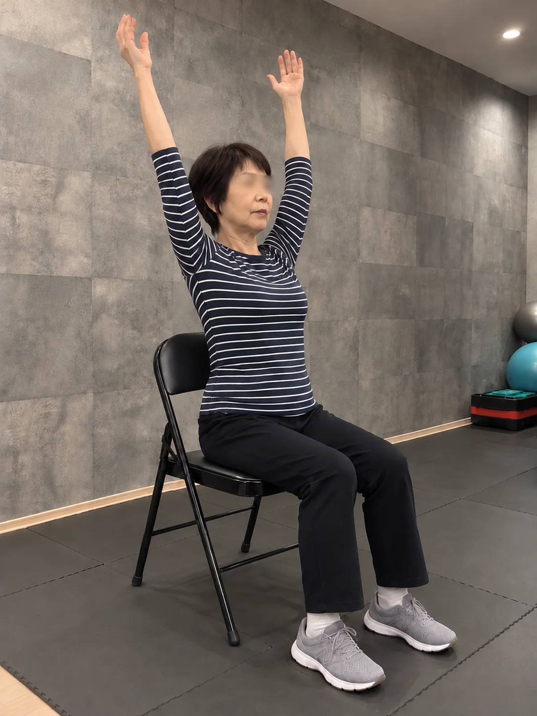 椅子に座って両腕を上げる運動をする女性
